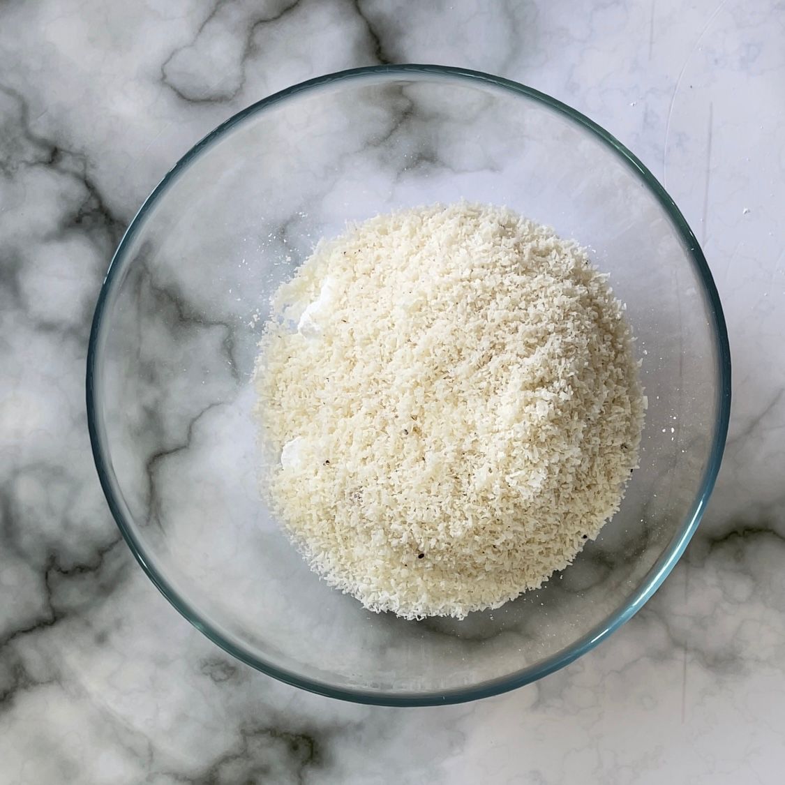 Una ciotola di vetro piena di polvere bianca su una superficie di marmo.