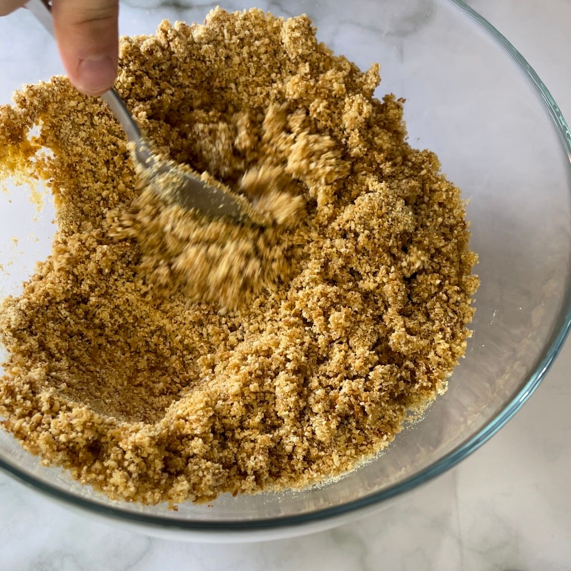 Una persona sta mescolando una sostanza marrone in una ciotola di vetro con un cucchiaio.