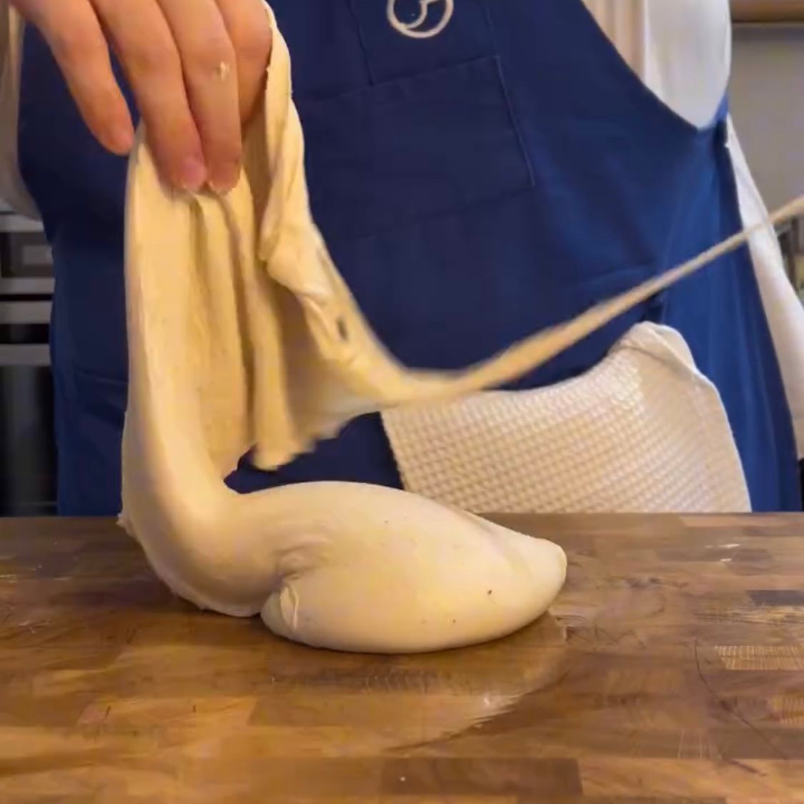 Una persona con un grembiule blu sta stendendo un pezzo di pasta