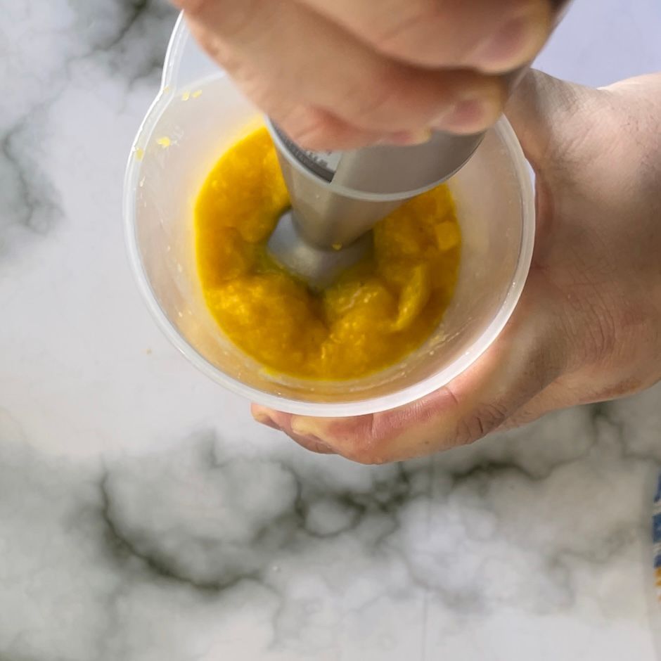 Una persona sta mescolando il cibo in una tazza con un frullatore.