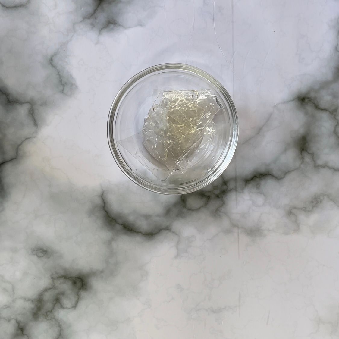Una piccola ciotola di vetro riempita con una sostanza bianca su una superficie di marmo.