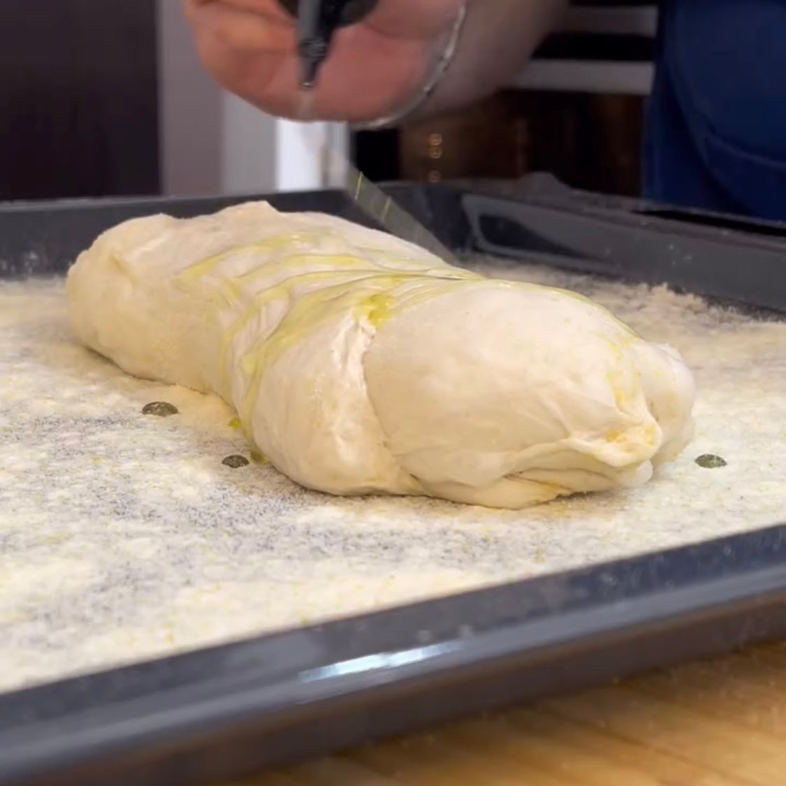 Una persona sta tagliando una pagnotta di pasta su un vassoio.