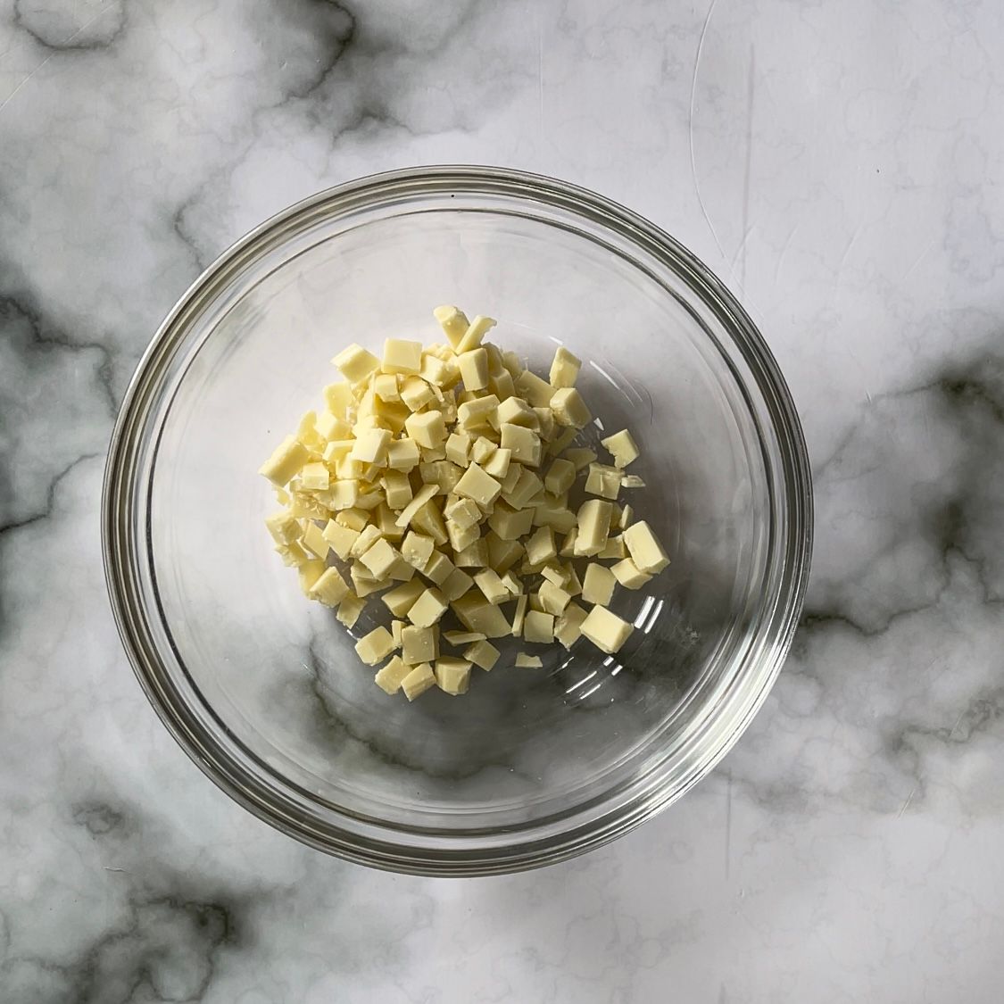 Una ciotola di vetro piena di cioccolato bianco tritato su una superficie di marmo.