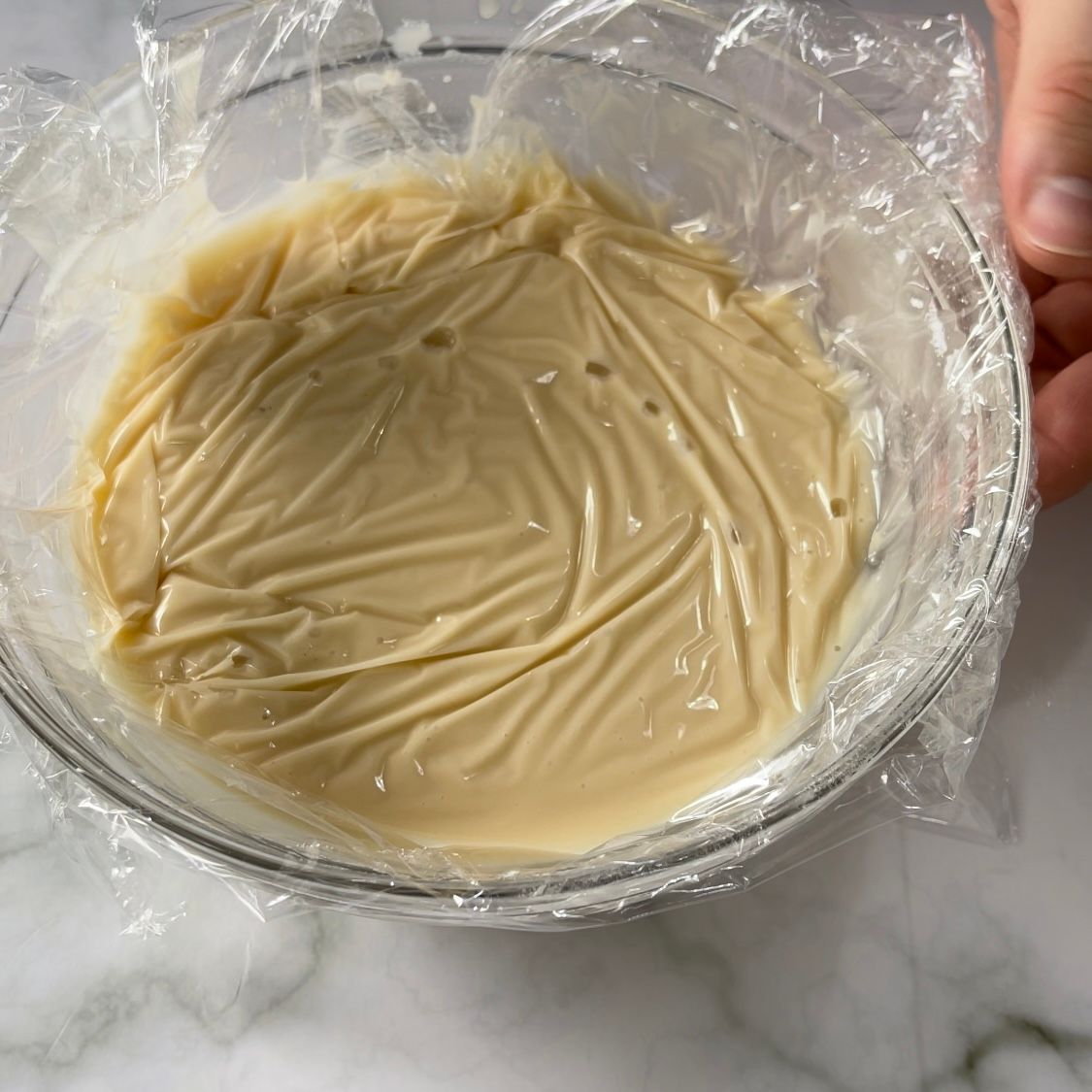 Una persona tiene in mano una ciotola di vetro ricoperta di pellicola trasparente.