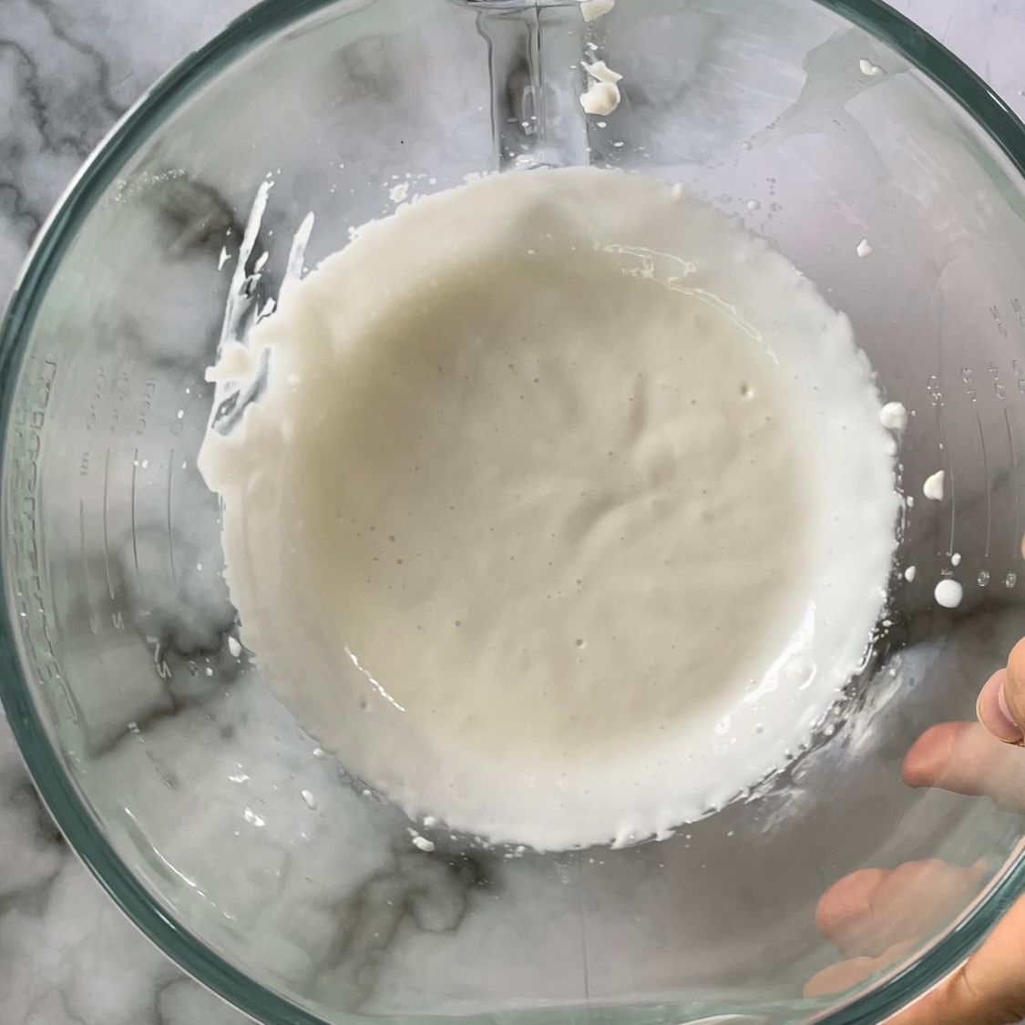 Una persona tiene in mano una ciotola di vetro piena di liquido bianco.