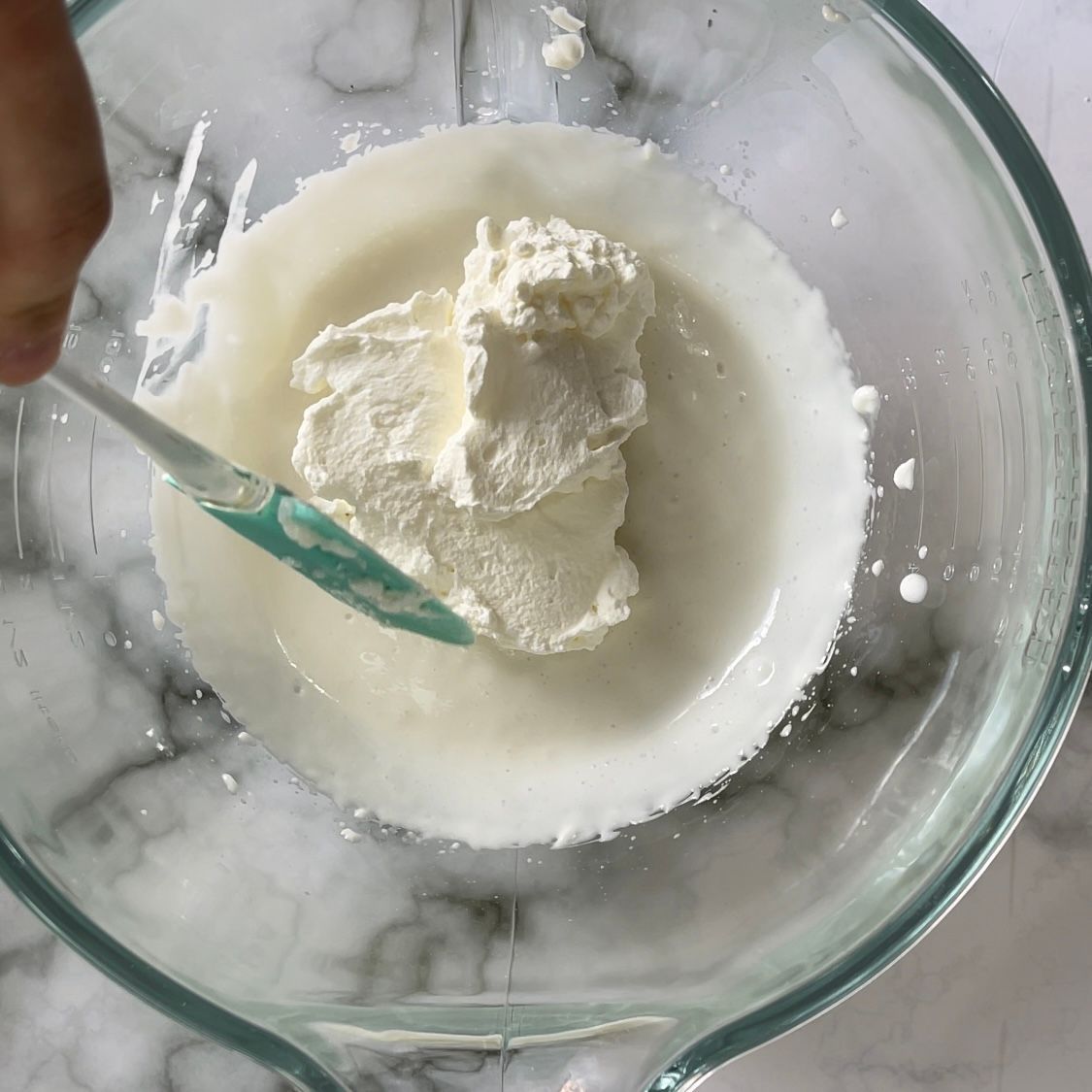 Una persona sta mescolando la panna montata in una ciotola di vetro con una spatola.