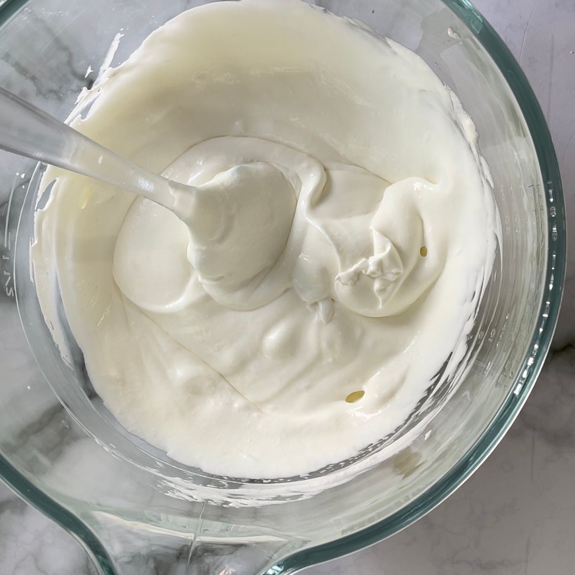 Una ciotola di vetro piena di glassa bianca con un cucchiaio dentro.