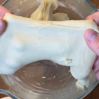 Una persona tiene in mano un pezzo di impasto sopra una ciotola piena di impasto.