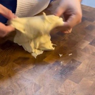 Una persona tiene in mano un pezzo di pasta su un tagliere di legno.