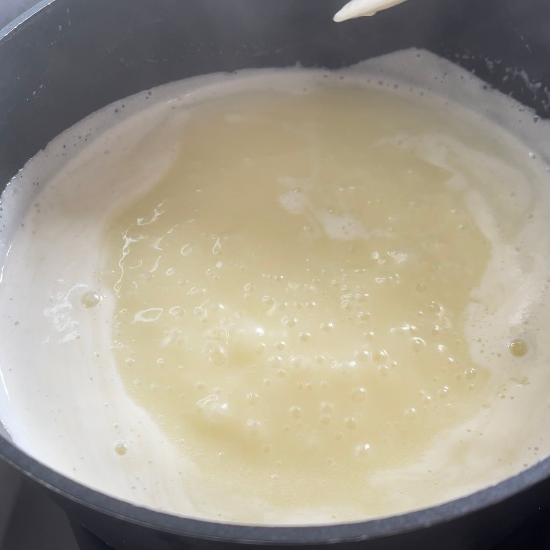 Una pentola contenente un liquido bianco viene mescolata con un cucchiaio di legno.