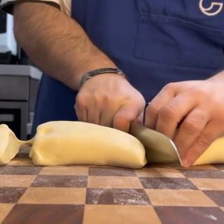 Un uomo che indossa un grembiule con la lettera g sopra sta tagliando un pezzo di pasta