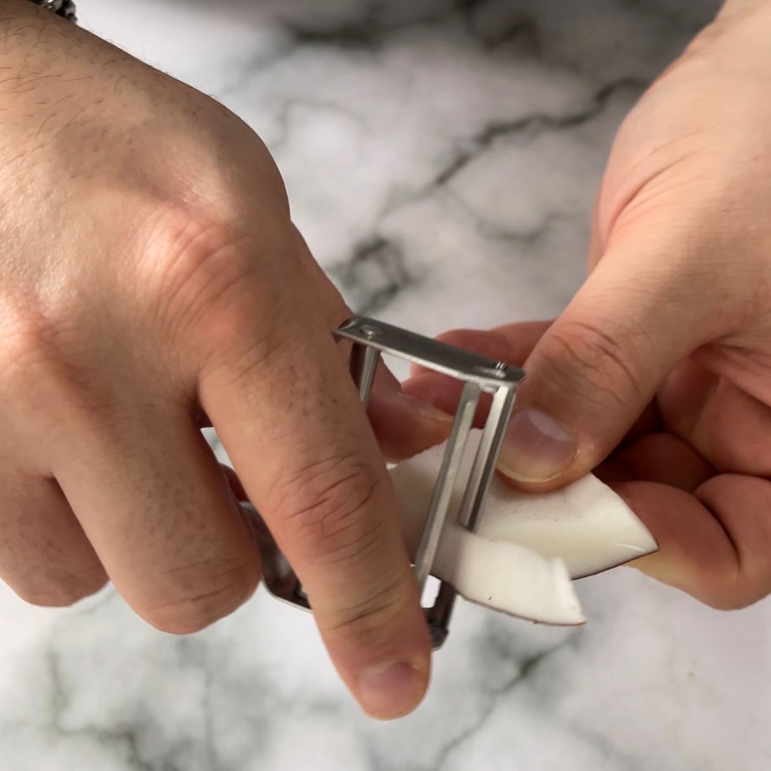 Una persona sta sbucciando una noce di cocco con un pelapatate in acciaio inossidabile