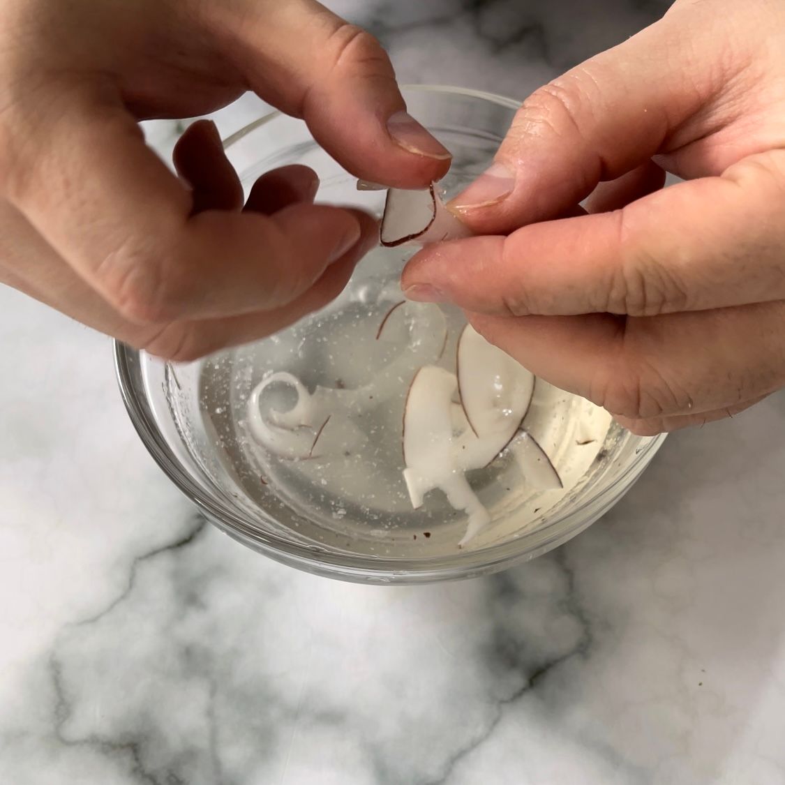 Una persona tiene in mano un pezzo di cocco in una ciotola d'acqua.