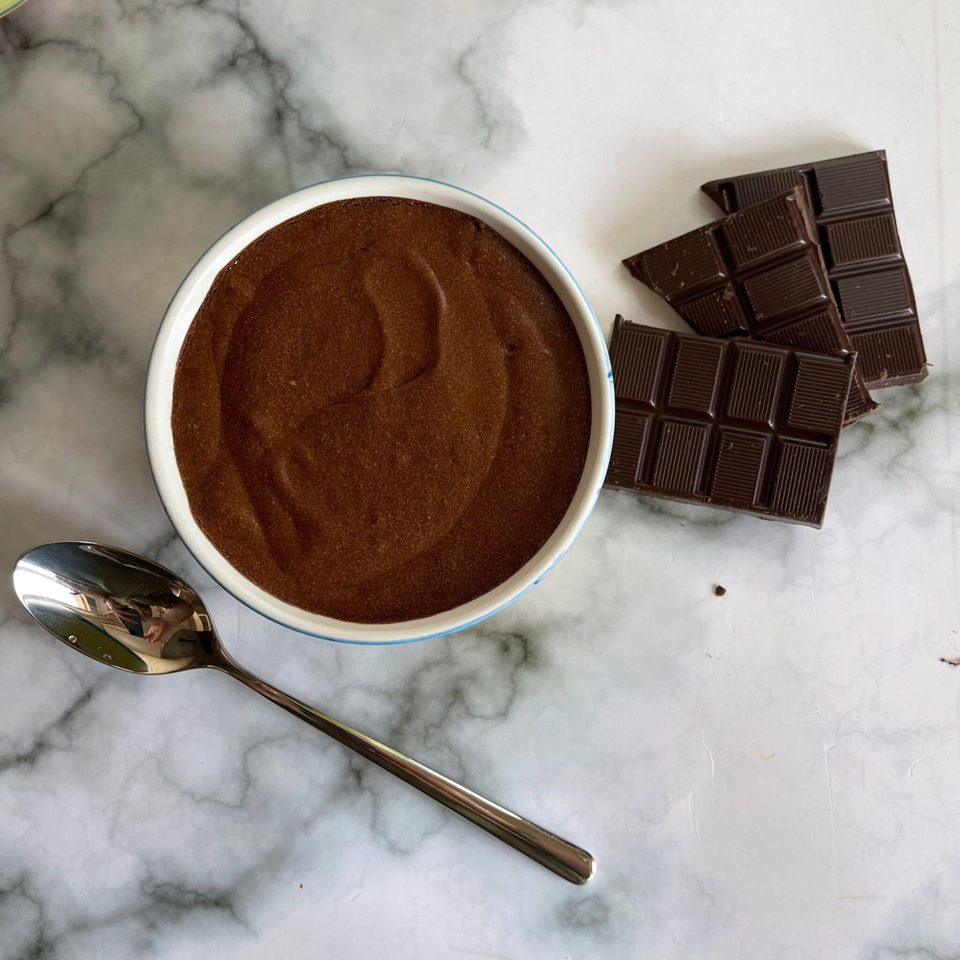 Una ciotola di budino al cioccolato accanto a un cucchiaio e delle barrette di cioccolato