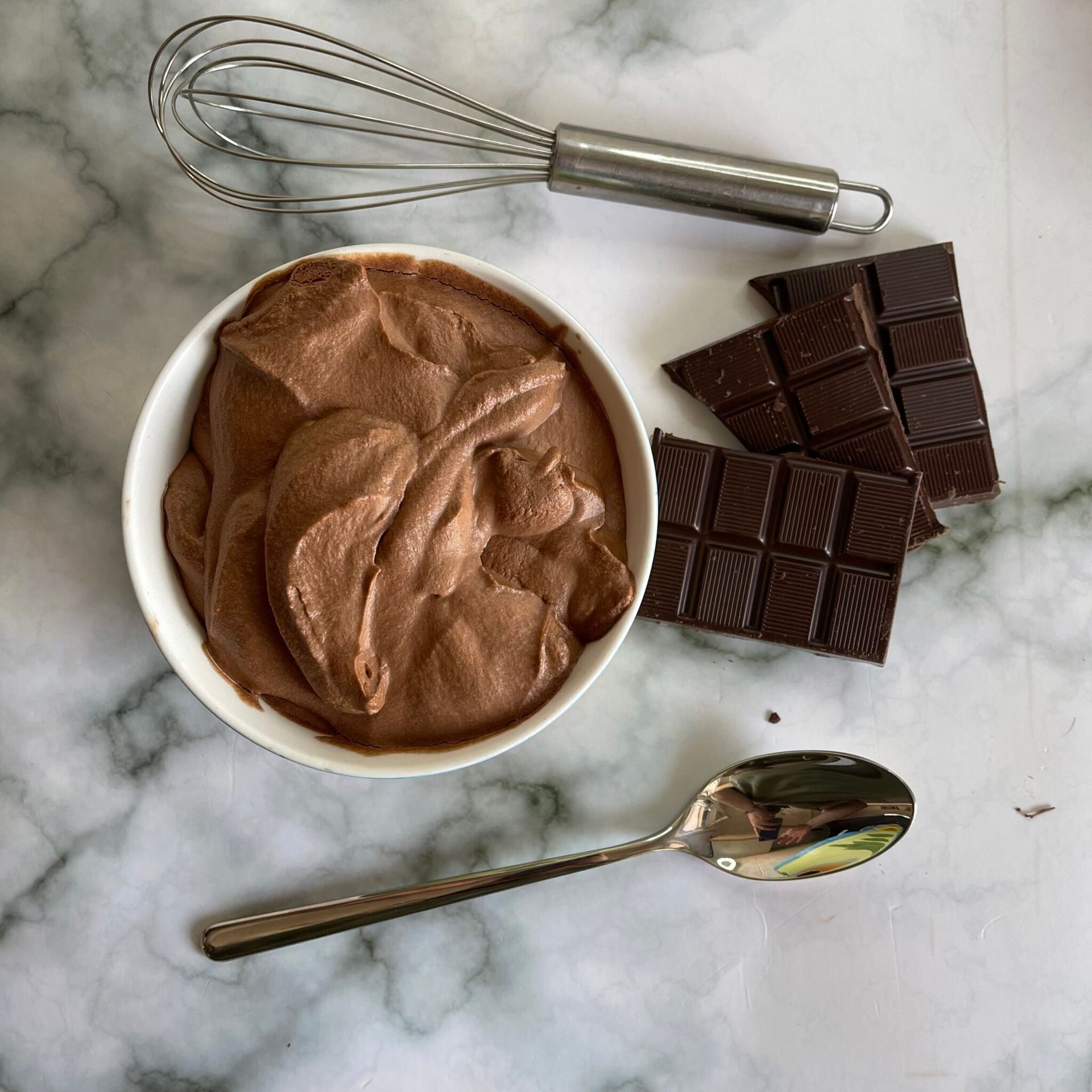 Una ciotola di mousse al cioccolato accanto a una frusta e delle barrette di cioccolato.