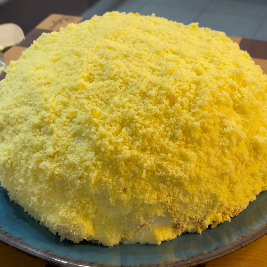 Una grande torta gialla è posta su un piatto blu su un tavolo.