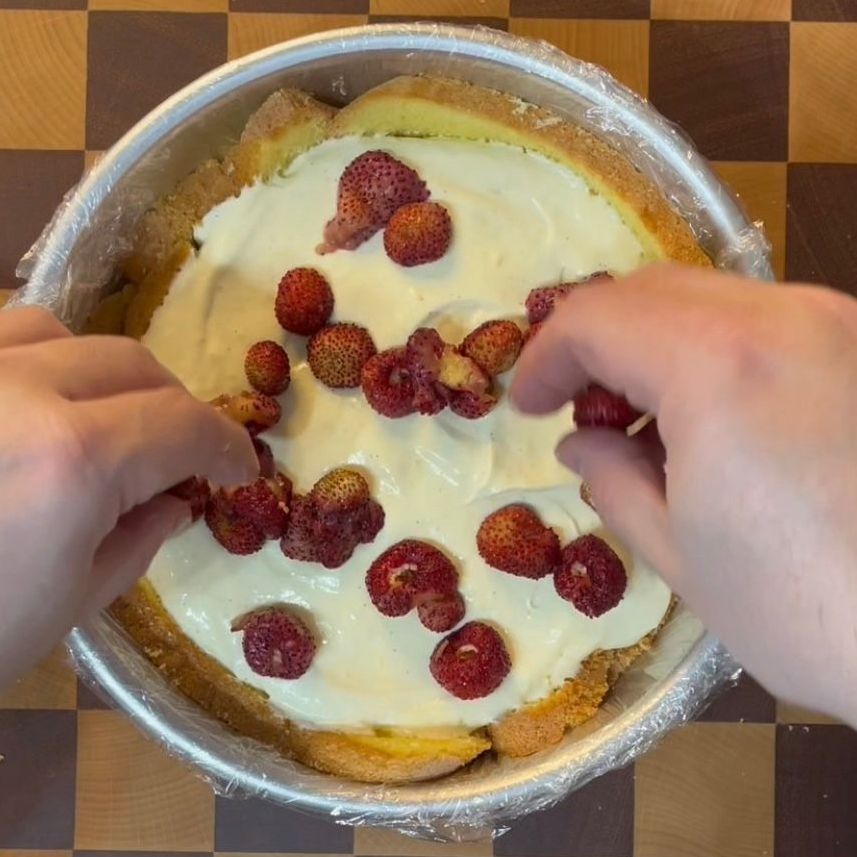 Una persona sta decorando una torta con lamponi e panna montata