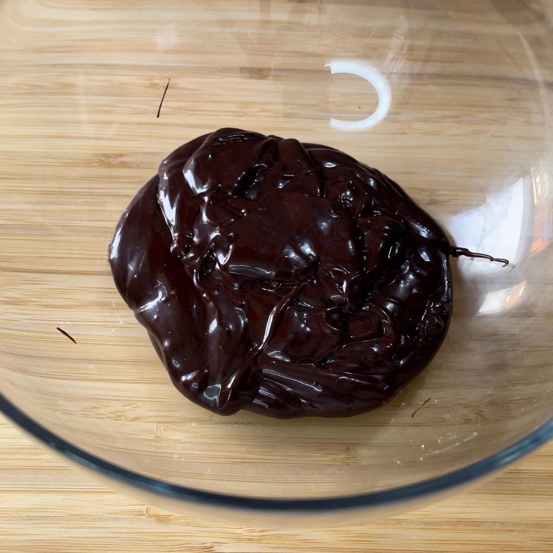 Una ciotola di vetro piena di salsa al cioccolato su un tavolo di legno.