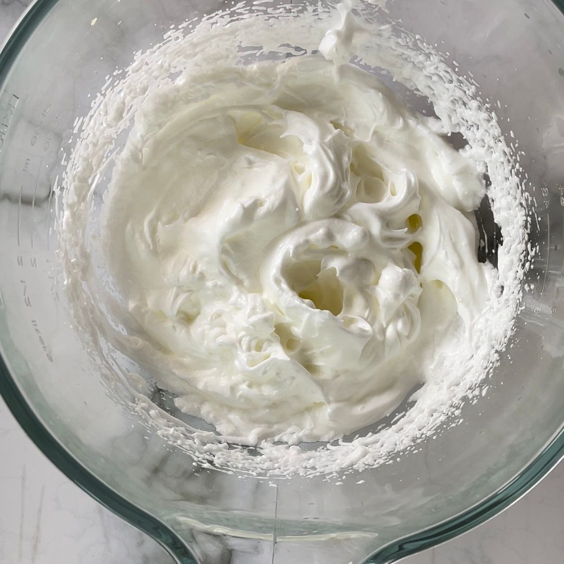 Una ciotola di vetro piena di panna montata su un tavolo.