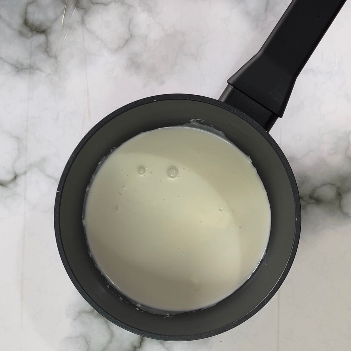 Una pentola nera piena di liquido bianco su una superficie di marmo