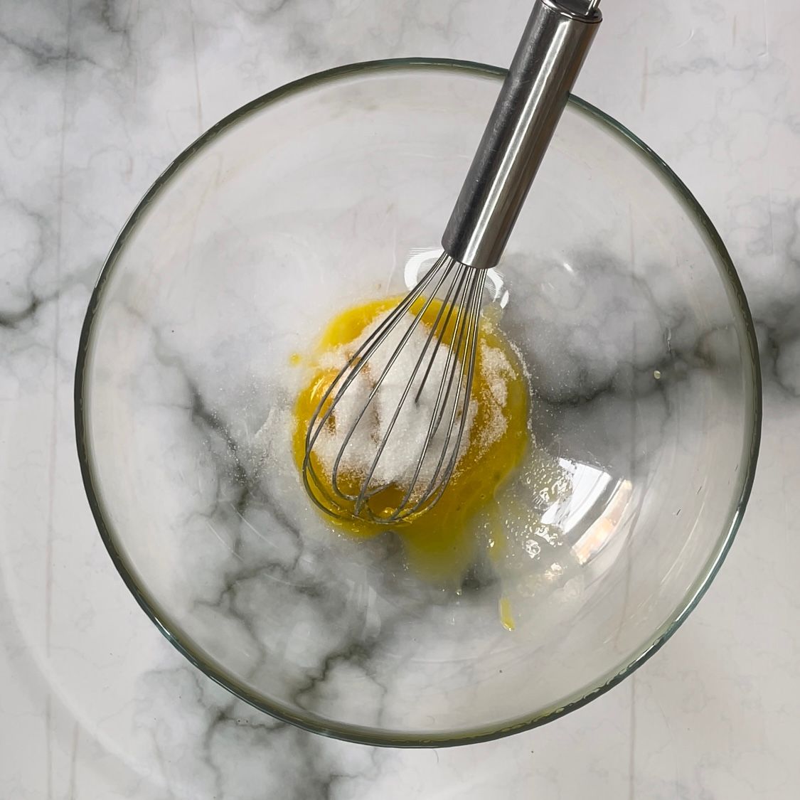 Una frusta è in una ciotola di vetro con un liquido giallo al suo interno.