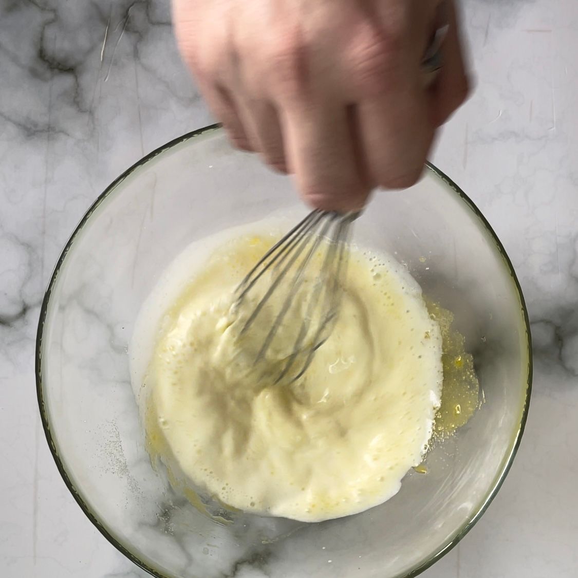 Una persona sta sbattendo un liquido giallo in una ciotola di vetro