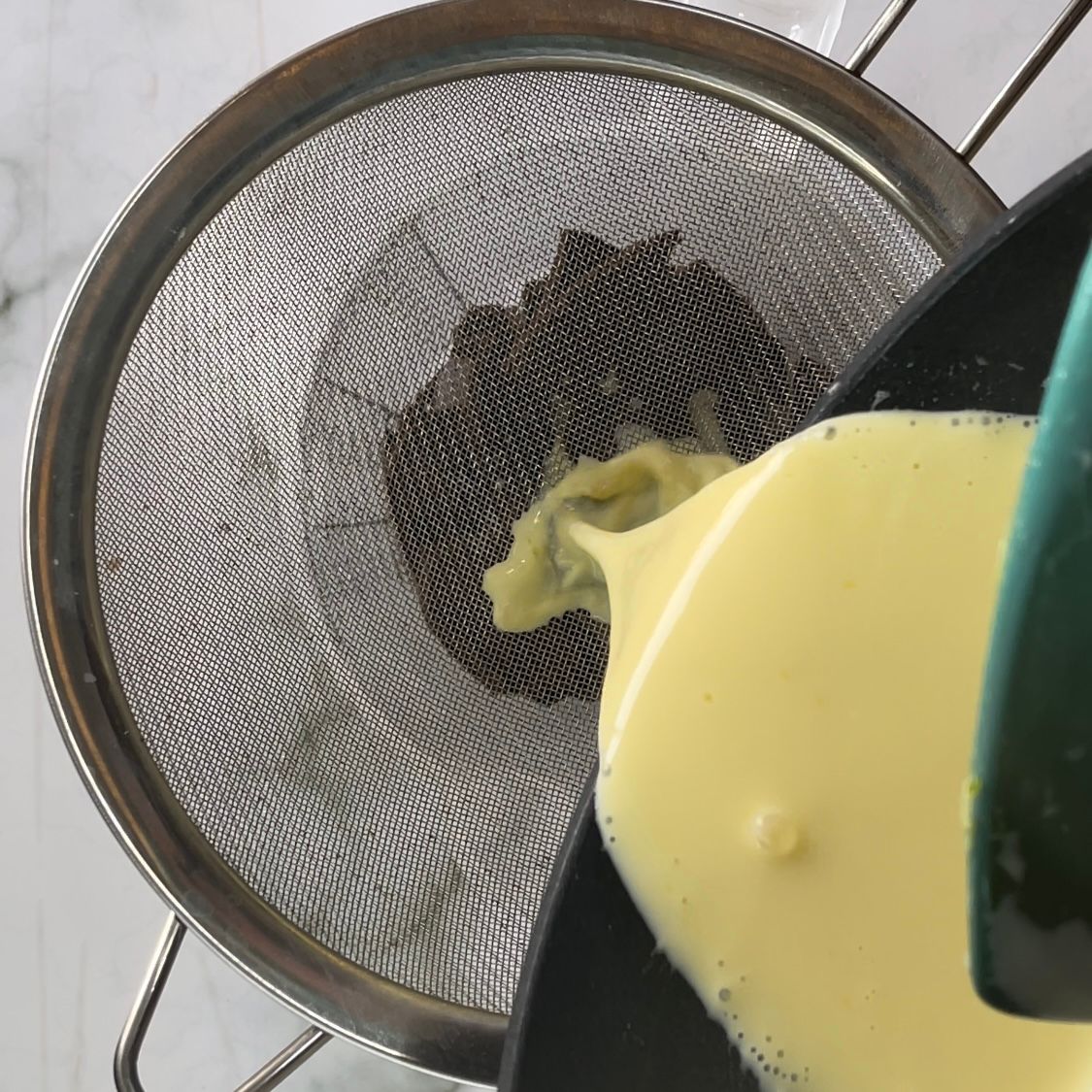 Un liquido giallo viene versato attraverso un colino in una pentola