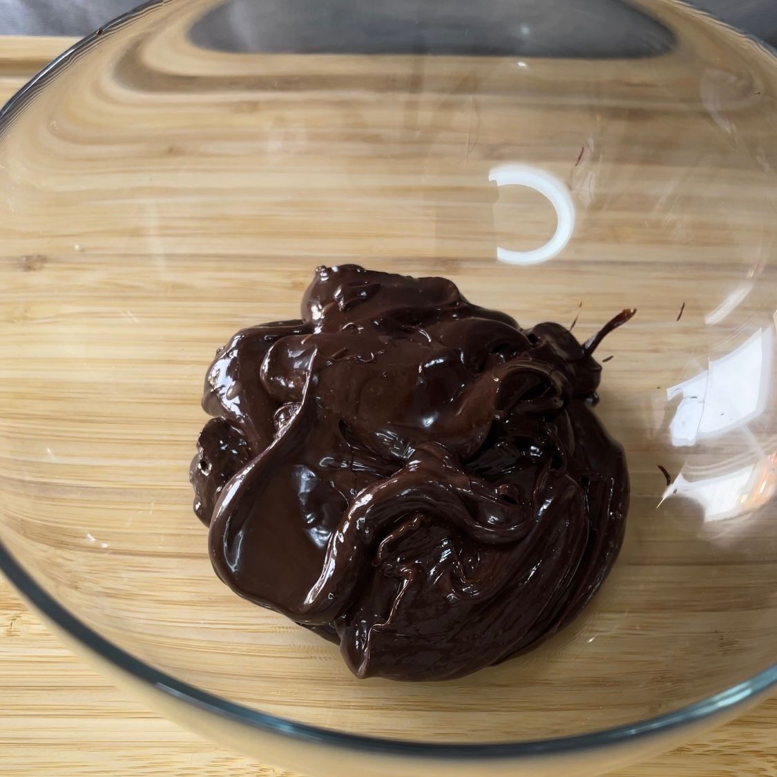 Una ciotola di vetro piena di salsa al cioccolato su un tagliere di legno
