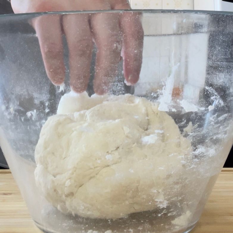 Una persona tiene in mano una palla di pasta in una ciotola di vetro