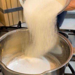 Una persona sta versando lo zucchero in una pentola di latte.