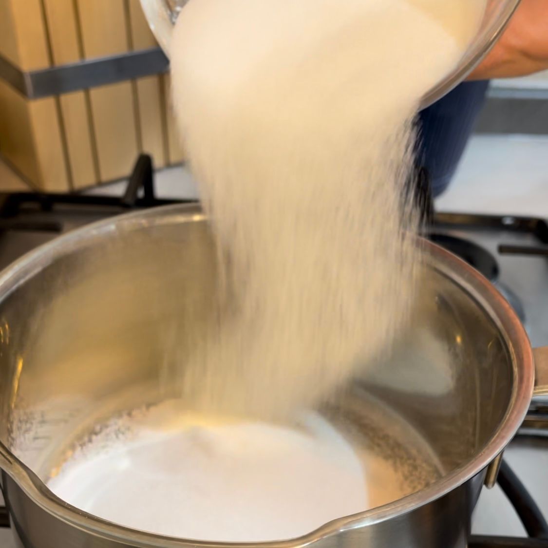 Una persona sta versando lo zucchero in una pentola di latte