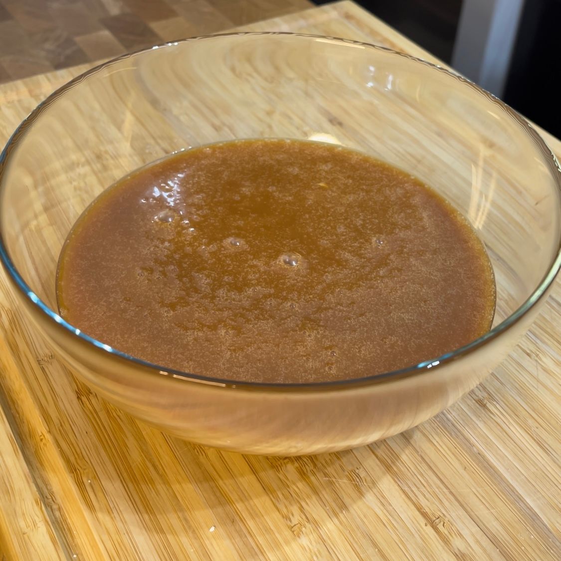 Una ciotola di liquido marrone è su un tavolo di legno