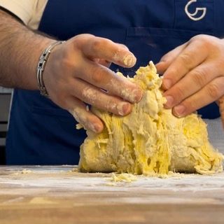 Un uomo con un grembiule sta impastando la pasta su un tagliere