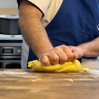 Un uomo con un grembiule blu sta impastando la pasta su un tagliere