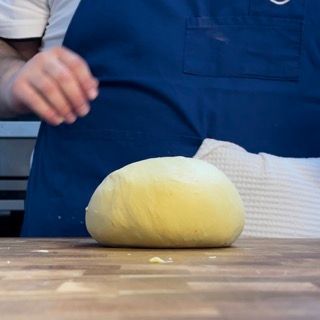 Una persona con un grembiule blu sta tagliando una palla di pasta