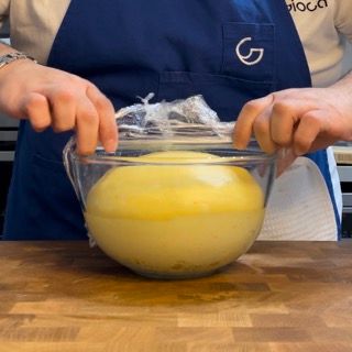 Una persona con un grembiule blu sta coprendo una ciotola di vetro con pellicola trasparente