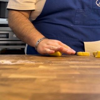 Un uomo con un grembiule blu sta tagliando un pezzo di pasta