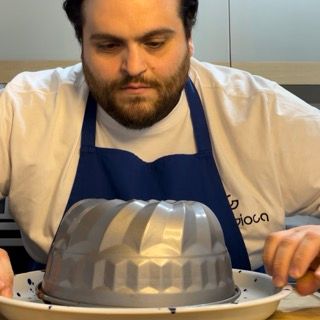 Un uomo che indossa un grembiule blu tiene una tortiera su un piatto