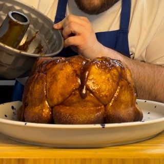 Un uomo con un grembiule sta versando la glassa su una torta Bundt