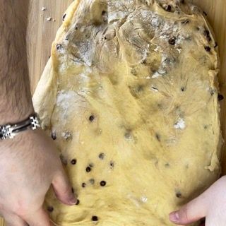 Una persona tiene in mano un pezzo di pasta su un tagliere di legno.