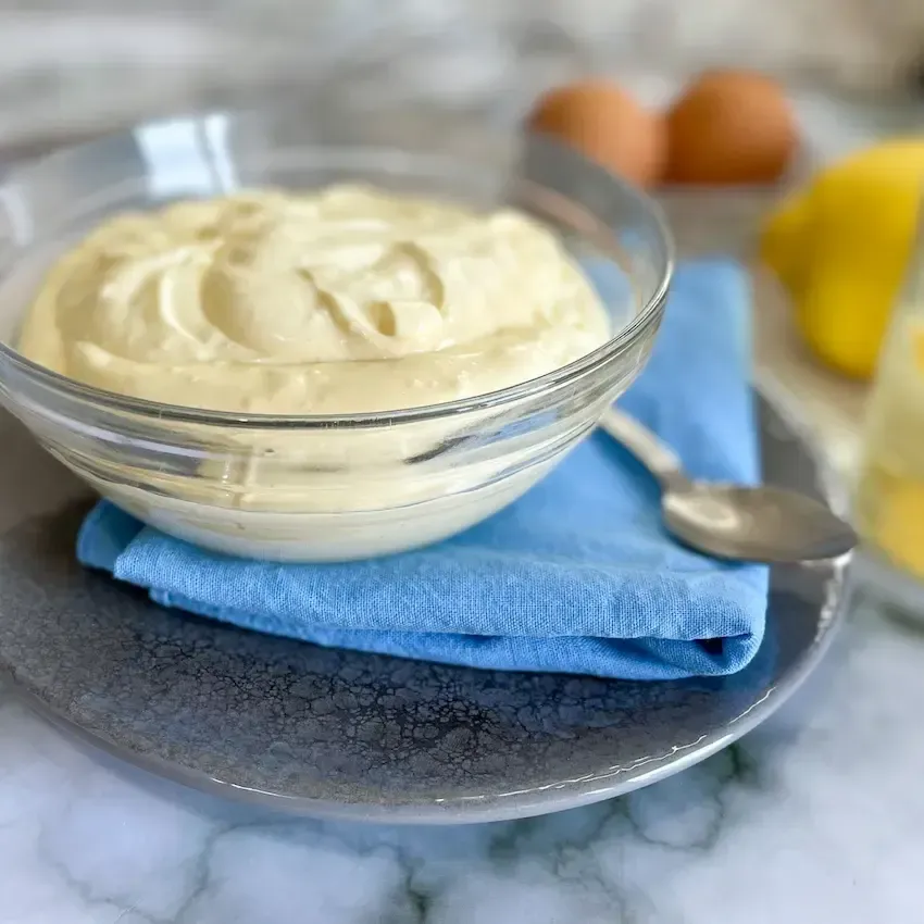 Maionese fatta in casa, densa e cremosa, in una ciotola di vetro con un cucchiaio.