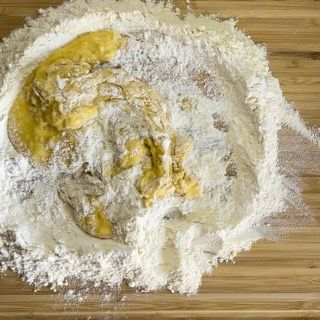 Un mucchio di farina e uova su un tagliere di legno.