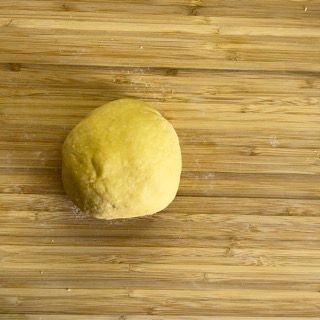 Una palla di pasta è appoggiata su un tagliere di legno.