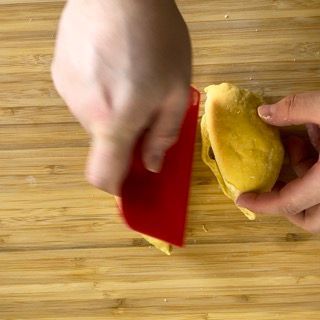 Una persona tiene in mano un pezzo di cibo su un tagliere di legno.