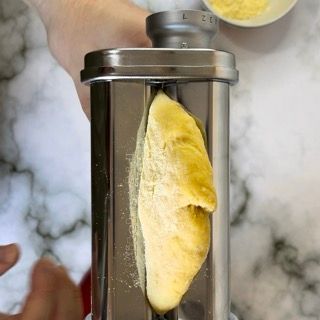Una persona tiene in mano una macchina per la pasta con un pezzo di impasto dentro.
