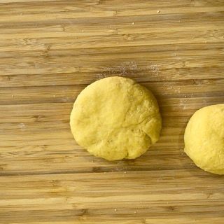 Due palline di pasta gialla sono appoggiate su un tagliere di legno.