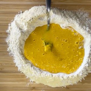 Un cucchiaio mescola un liquido giallo in un mucchio di farina.