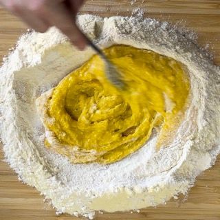 Una persona sta mescolando un liquido giallo in un mucchio di farina.