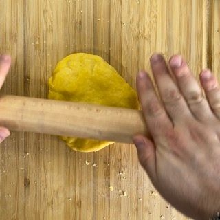 Una persona sta stendendo la pasta con un mattarello di legno su un tagliere di legno.