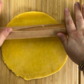 Una persona sta stendendo un pezzo di pasta gialla con un mattarello di legno.